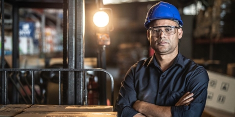 Man with a blue hard hat and goggles crossing his arms.