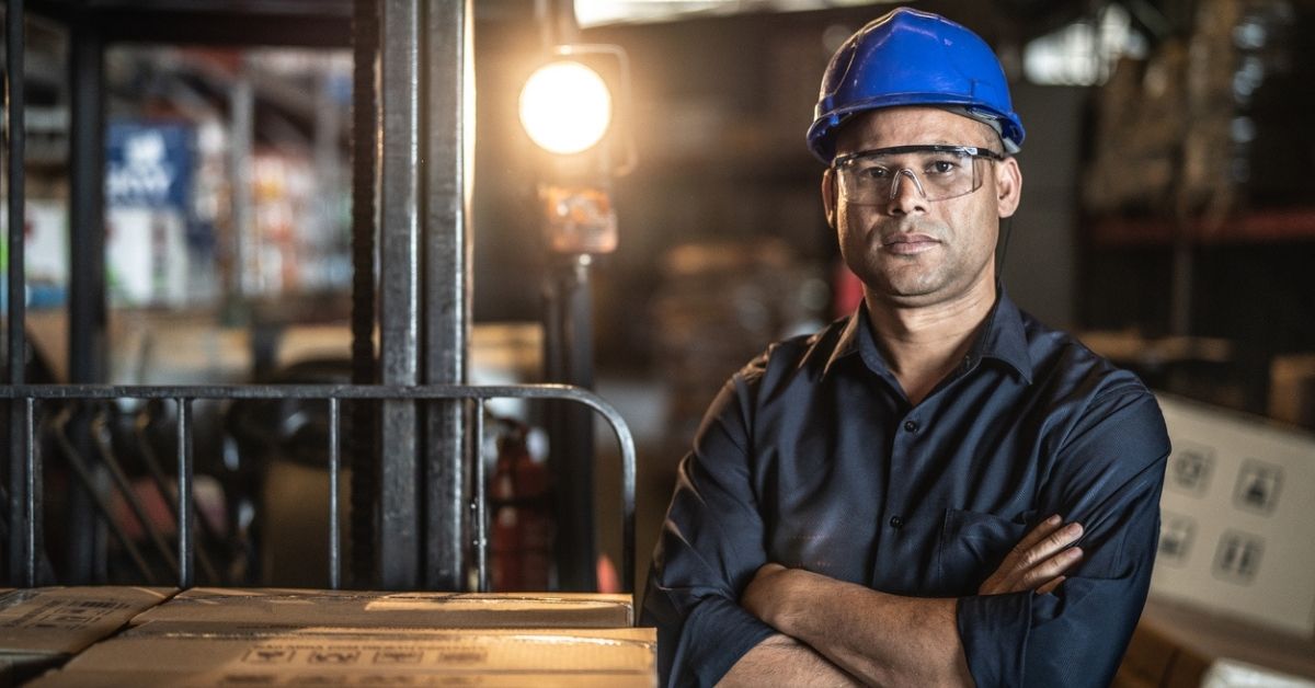 Man with a blue hard hat and goggles crossing his arms.
